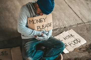 Beggars sitting under the bridge with a sign, please money.