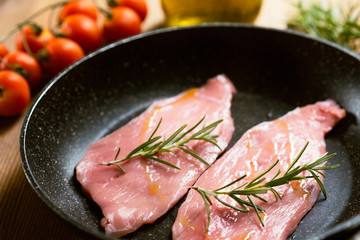 Raw  Veal Meat Steaks on a pan, tomatoes, rosemary, oil, garlic. Wooden background, side view 