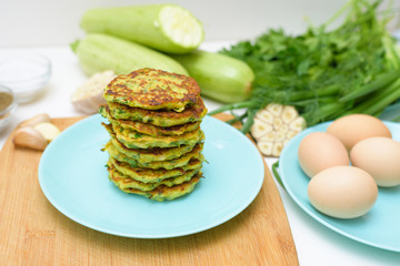 veggie fried pancakes with zucchini and greens on a blue plate on a light background on a wooden Board . recipe with the addition of eggs and flour. top view, selective focus, space for text