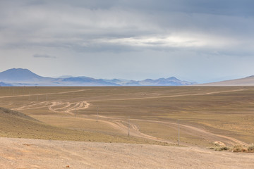 Fototapeta na wymiar Typical view of Mongolian landscape. Winding dirt road through lush rolling hills of Central Mongolian steppe. Mongolian Altai