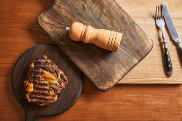 top view of tasty grilled steak served on wooden boards with cutlery and salt mil