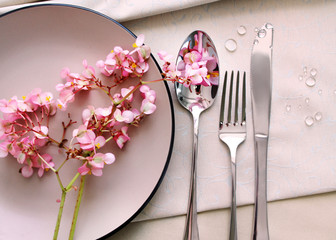 

cutlery on a serving table, close up. pink begonia flowers on a plate as a table decor. table setting details.