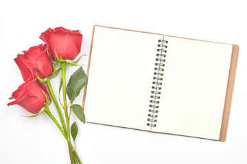 Top view shot of empty blank notebook diary and red roses on white table