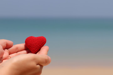 Sea vacation and love on a sandy beach, red knitted heart in a female hands against the blue water....