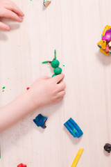 a small child sculpts a caterpillar from green plasticine on a wooden table, the development of fine motor skills of hands than to entertain a child at home, stay at home