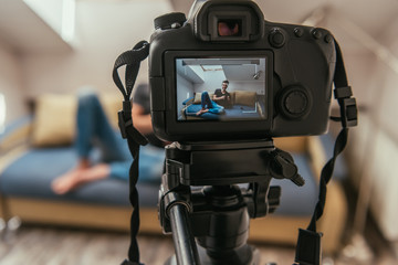 selective focus of digital camera with young vlogger knitting on sofa at home