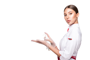 Beauty female doctor cosmetologist in medical gloves holding the bottle with lotion and presents an advertisement product. Model woman in medical robe isolated on white background