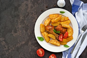 Thigh and chicken leg baked with potato wedges on a light ceramic plate on a dark concrete background. Recipes with potatoes. Thanksgiving Recipes