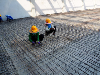 workers hands using steel wire and pincers to secure rebar before concrete is poured over it.
