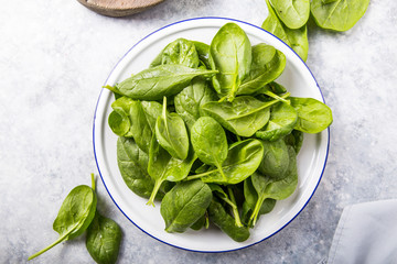 Baby spinach leaves in bowl on grey concrete background, top view, copy space. Clean eating, detox, diet food ingredient