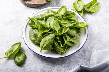 Baby spinach leaves in bowl on grey concrete background, top view, copy space. Clean eating, detox,...