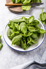 Baby spinach leaves in bowl on grey concrete background, top view, copy space. Clean eating, detox, diet food ingredient