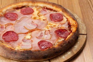 hearty italian pizza on a wooden board. crispy pizza with ham, bacon, salami and cheese sausages