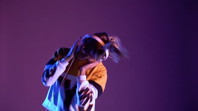 Cool happy hooded gen z hipster teen girl wearing headphones and glasses listening new cool dj pop 90s music playlist songs podcast dancing alone in purple violet color neon studio light. Slow motion