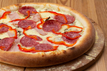 hearty italian pizza on a wooden board. crispy pizza with ham, pepper, salami and cheese sausages
