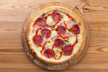 hearty italian pizza on a wooden board. crispy pizza with ham, pepper, salami and cheese sausages