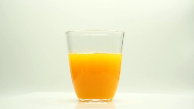 Vaso de zumo de naranja girando sobre fondo blanco