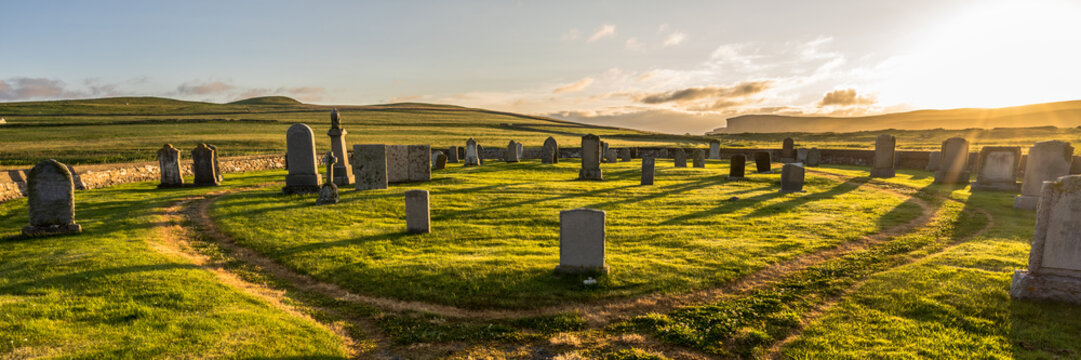 panorama of old hillswick cemetery full of tombstones on the Shetland (Scotland, UK) on a magical sunset with dramatic warm light and a green meadow