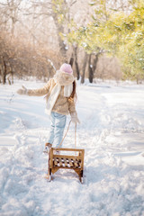 Beautiful girl of 12 years old with curly long hair runs through the winter forest with wooden sledges