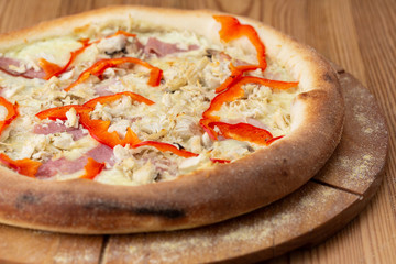 hearty italian pizza on a wooden board. pizza with chicken, pepper, ham and cheese