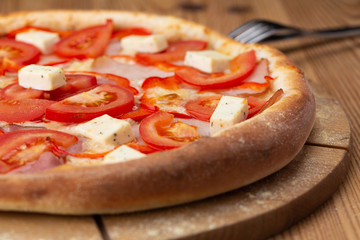 hearty italian pizza on a wooden board. pizza with tomatoes, peppers, ham and hard cheese