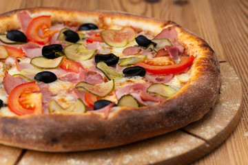 hearty italian pizza on a wooden board. .pizza with ham, tomatoes, pickles and olives