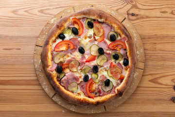 hearty italian pizza on a wooden board. .pizza with ham, tomatoes, pickles and olives