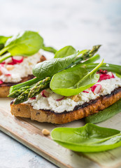 Vegan sandwich with tofu, spinach, radish, asparagus,  and green dressing on the board.