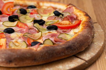 hearty italian pizza on a wooden board. .pizza with ham, tomatoes, pickles and olives