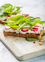 Vegan sandwich with tofu, spinach, radish,   and green dressing on the board.