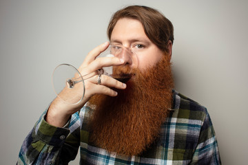 A red-bearded man drinking wine from a large glass. A vine tasting at home. Sommelier for yourself at home. A man with a big beautiful beard.