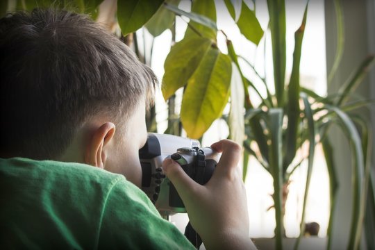 A child with a camera in his hands on the background of a window with indoor plants