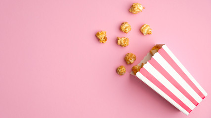Obraz premium Striped box with caramel popcorn on pink background. Flat lay, top view.