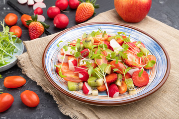 Vegetarian fruits and vegetables salad of strawberry, kiwi, tomatoes, microgreen sprouts on black concrete background. Side view.