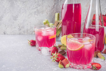 Homemade rhubarb and strawberry alcohol cocktail. Rhubarb liquor or gin, on a gray background with fresh rhubarb, strawberries, lemon, mint