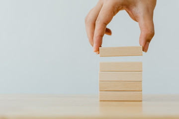 Hand arranging wood block stacking on top with wooden table. Business concept for growth success...
