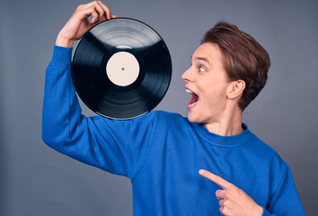 Surprised young man in a blue sweater and a turntable in his hands.