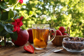 useful herbal green tea in a glass mug, strawberries in a basket, red apples, flowers of a climbing plant clematis, concept of lifestyle, flower tea on the terrace, seasonal