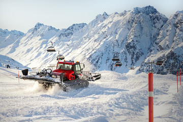 Red modern snowcat ratrack with snowplow snow grooming machine preparing ski slope piste hill at alpine skiing winter resort Ischgl in Austria. Heavy machinery mountain equipment track vehicle