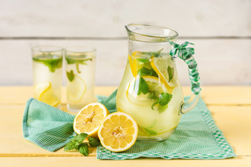 Lemonade with lemon and mint in a jug on a yellow rustic table.