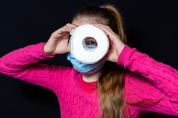 a teenage girl in a pink sweater and protective mask holds toilet paper and looks through a hole in it.