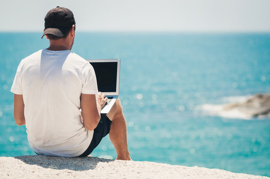 Young man freelancer works remotely on a high coastal cliff overlooking the Gulf of Thailand.