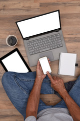 High angle of a male sitting on the floor with his Electronic Devices - Smartphone, Laptop Computer and Tablet with blank white screens ready for your copy or graphic.