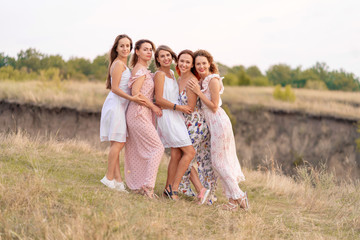 A cheerful company of beautiful girls friends enjoy the company and have fun together in a picturesque place of green hills.