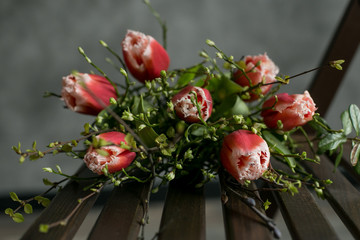 Tulips on the chair. Wooden stool with flowers. Present at the birthday. Forgotten bouquet on the chair in the restaurant. Bouquet at the bench.