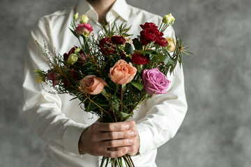 Beautiful bouquet in man's hands on a background of gray wall. Flowers art design. Man in white...