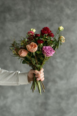 Beautiful bouquet in man's hands on a background of gray wall. Flowers art design. Man in white...