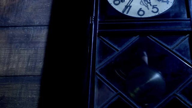 Close up of antique pendulum clock on wooden wall at night