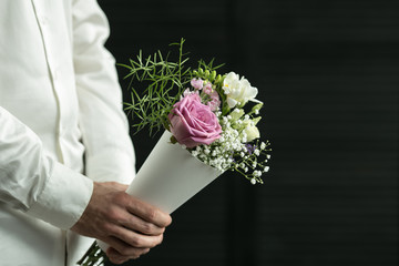 Beautiful bouquet in man's hands on a background of gray wall. Flowers art design. Man in white...