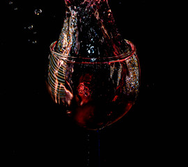 Close-up of glass cup with water and strawberry falling into splash, with black background.